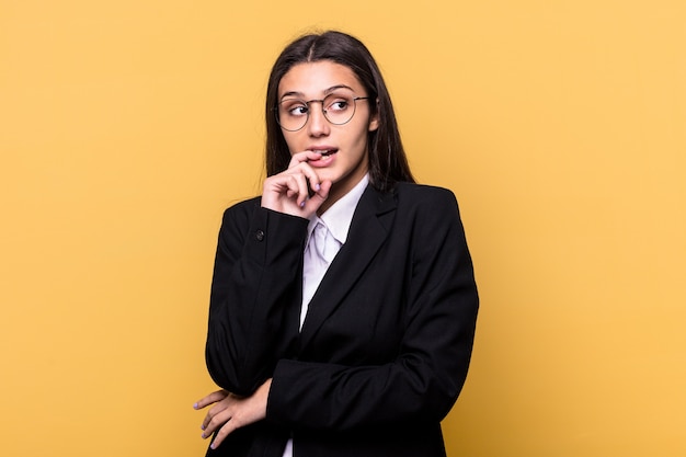 Young Indian business woman isolated on yellow wall relaxed thinking about something looking at a copy space.