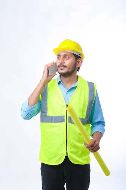 Young indian engineer wearing hardhat and talking smartphone on white background.