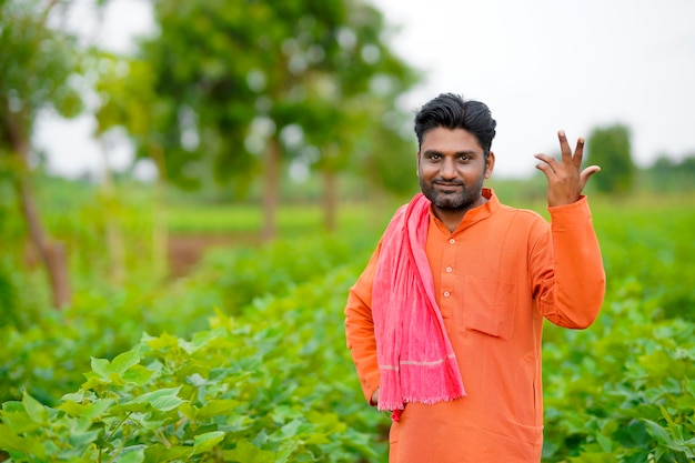 Young indian farmer standing in cotton agriculture field.