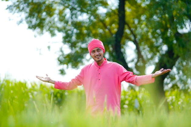 Young indian farmer standing his wheat field and giving happy expression