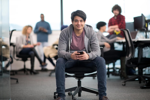 young indian male software developer using mobile phone writing messages while having break at modern creative startup office