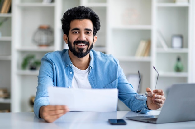 Young indian male working with papers and laptop at home office