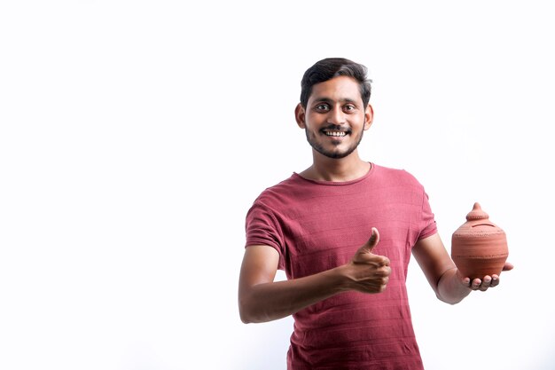 Young indian man holding clay piggy bank in hand over white background.