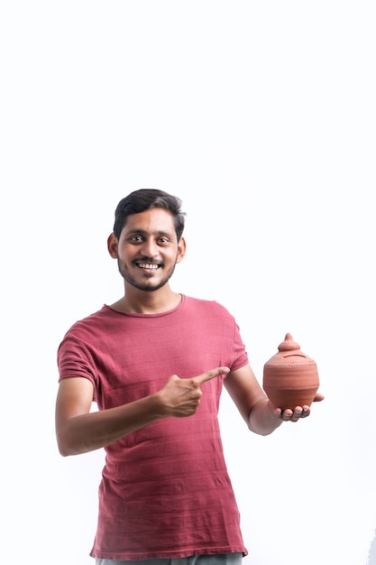 Young indian man holding clay piggy bank in hand over white background.