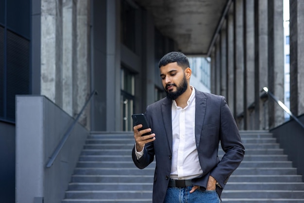 Young indian man real estate agent broker standing near office outside and using phone waiting for