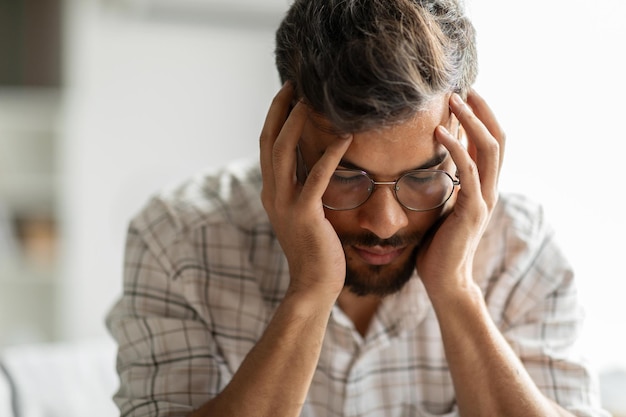 Photo young indian man suffering from migraine feeling unwell touching head with closed eyes suffering