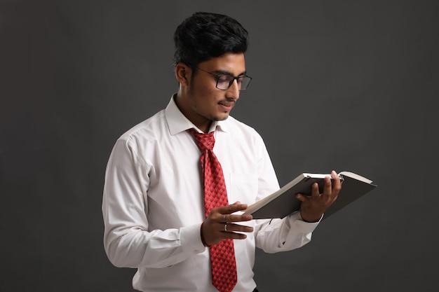 Young indian successful business man or executive wearing spectacles and reading book over dark background.