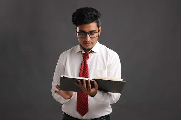 Young indian successful business man or executive wearing spectacles and reading book over dark background.