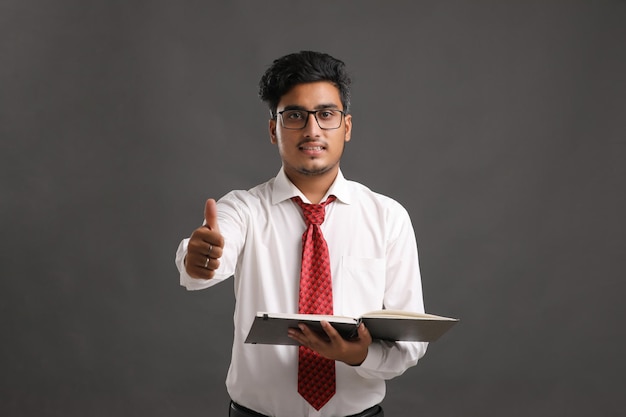 Young indian successful business man or executive wearing spectacles and reading book over dark background.