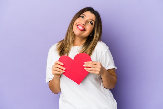 Young indian woman holding a valentines day heart isolated dreaming of achieving goals and purposes