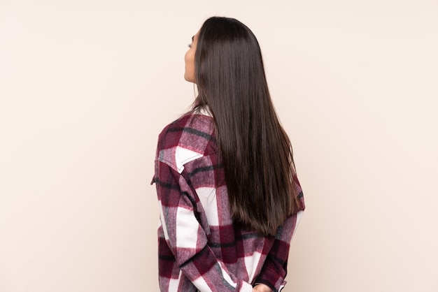 Young Indian woman isolated on beige in back position and looking back