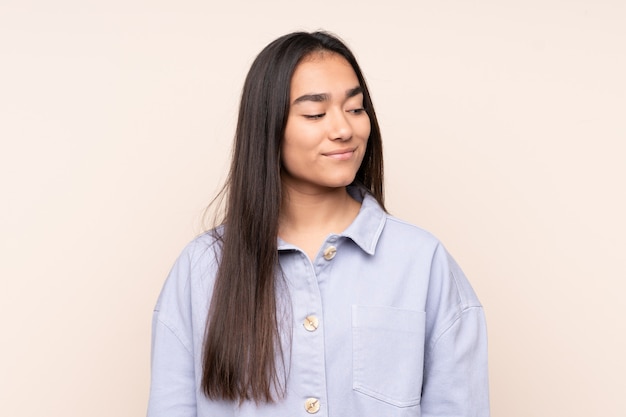 Young Indian woman isolated on beige wall having doubts while looking side