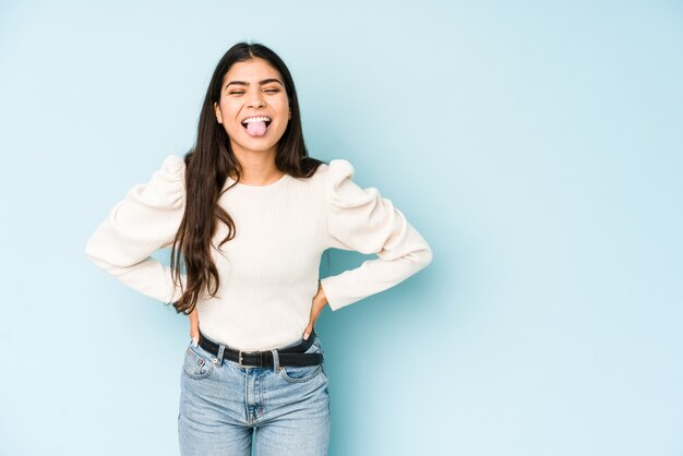 Young indian woman isolated on blue funny and friondly sticking out tongue.