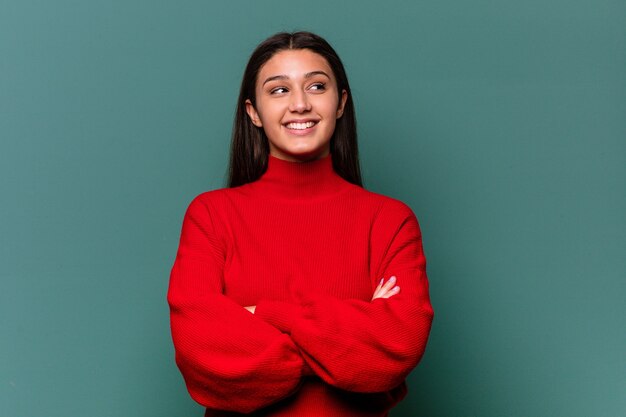 Young Indian woman isolated on blue wall smiling confident with crossed arms