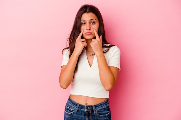 Young Indian woman isolated on pink background crying, unhappy with something, agony and confusion concept.