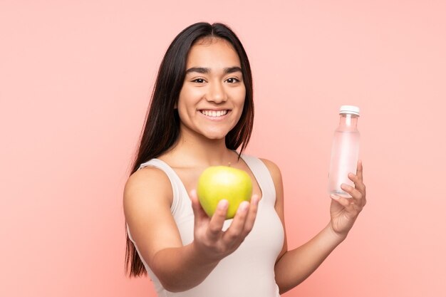 Young Indian woman isolated on pink background with an apple and with a bottle of water