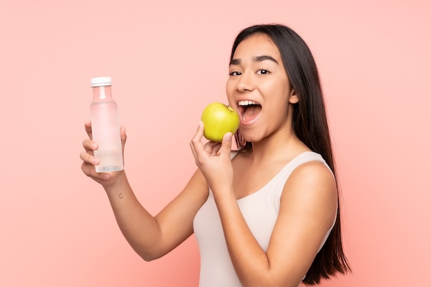 Young Indian woman isolated on pink with an apple and with a bottle of water