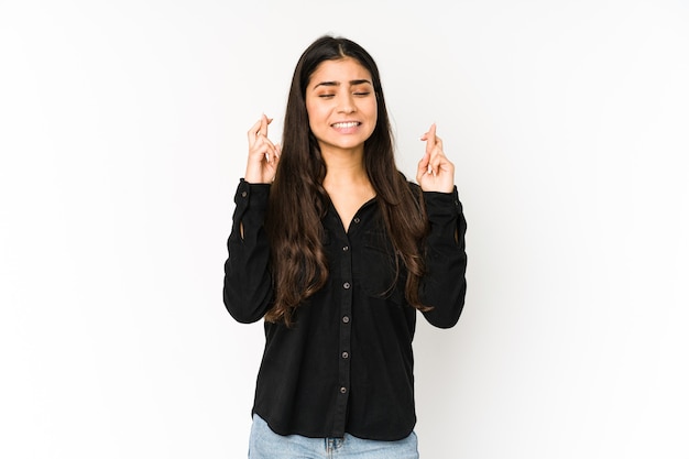 Young indian woman isolated on purple background crossing fingers for having luck