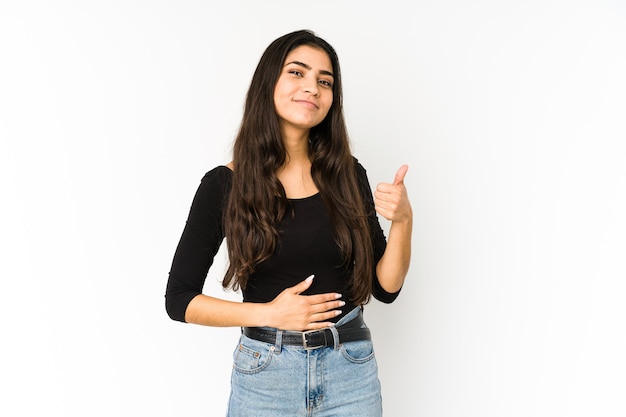 Young indian woman isolated on purple touches tummy, smiles gently, eating and satisfaction concept.