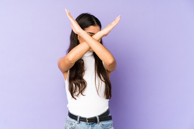 Young indian woman isolated on purple wall keeping two arms crossed, denial concept.