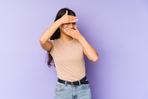 Young indian woman on purple wall blinking through fingers