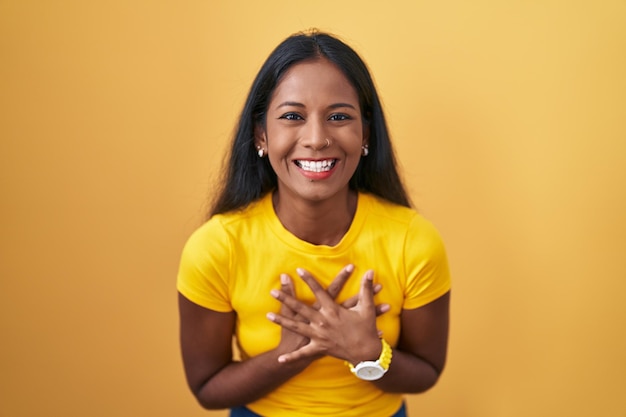 Young indian woman standing over yellow background smiling and laughing hard out loud because funny crazy joke with hands on body