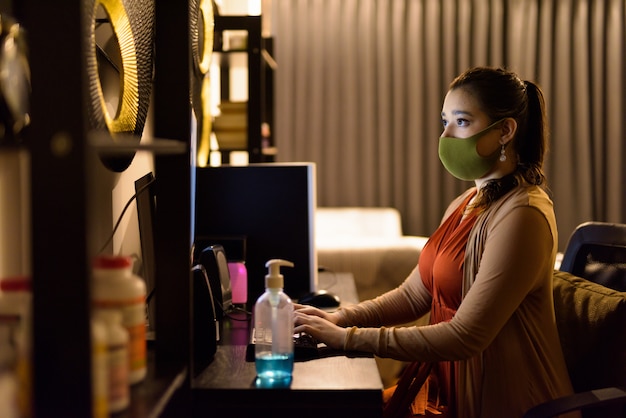 Young Indian woman wearing mask while working from home late at night