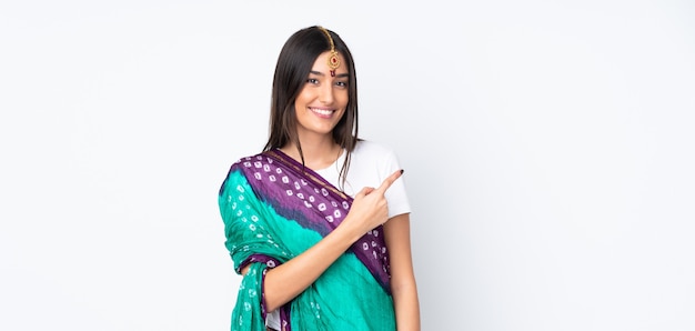 Young Indian woman on white wall pointing to the side