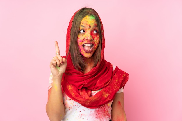 Young Indian woman with colorful holi powders on her face isolated on pink wall intending to realizes the solution while lifting a finger up