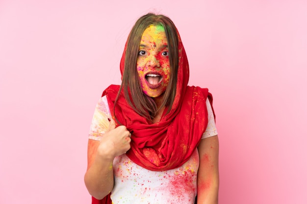 Young Indian woman with colorful holi powders on her face isolated on pink wall pointing to oneself