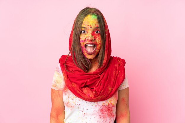 Photo young indian woman with colorful holi powders on her face on pink wall with surprise facial expression