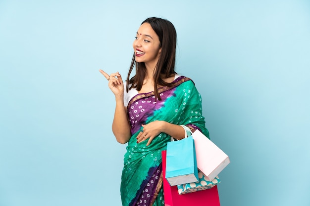 Young Indian woman with shopping bags intending to realizes the solution while lifting a finger up