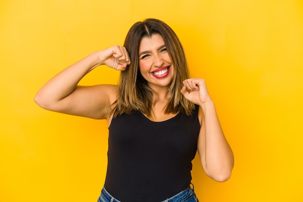 Young indian woman on yellow raising fist after a victory, winner concept.