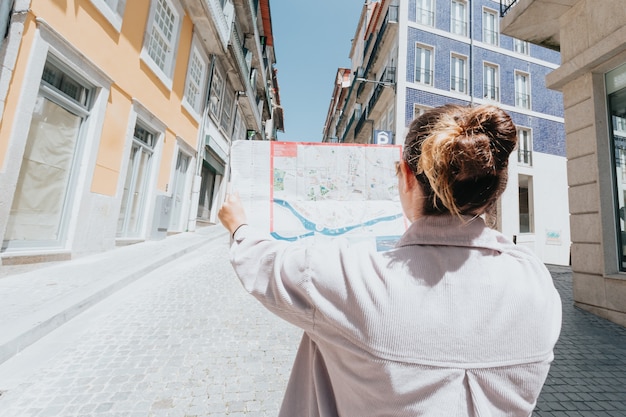 Photo young indie woman using a map in the middle of a street in europe, sunny day, summer day, travel concepts, new horizons, copy space