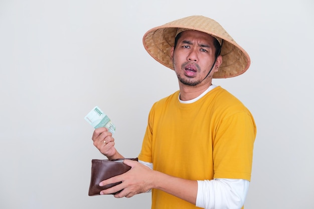 Young Indonesian farmer showing sad expression when taking money from his wallet