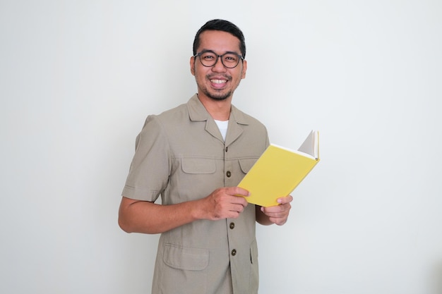 Young Indonesian teacher smiling happy at the camera while holding a book