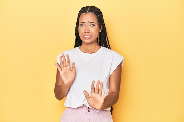 Young Indonesian woman on yellow studio backdrop rejecting someone showing a gesture of disgust