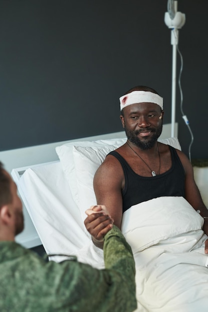 Young injured soldier looking at his friend during handshake in hospital