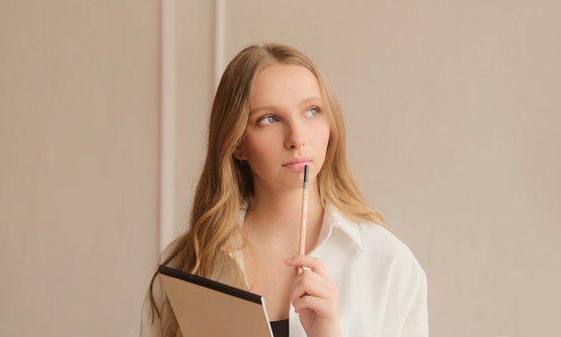 Young inspired woman pensively thinks and making notes in paper notebook