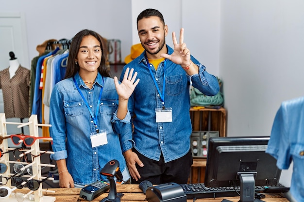 Young interracial people working at retail boutique showing and pointing up with fingers number eight while smiling confident and happy.