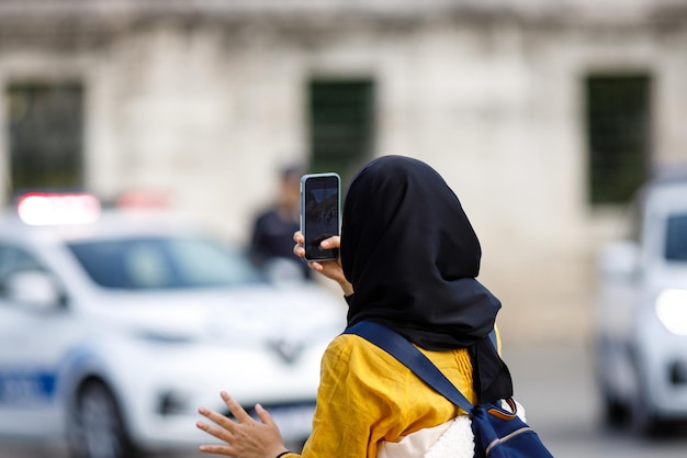 Young Islamic woman taking photos on phone back view Shooting video with cell phone camera using smartphone to take pictures outdoor Tourist photographing landscape