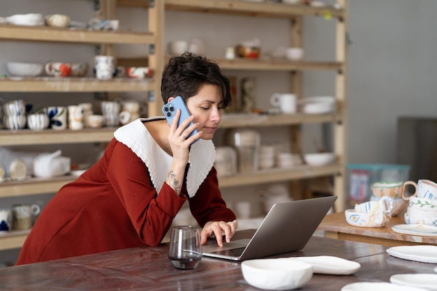 Young italian female artisan artist ordering materials for ceramic work by phone in art studio