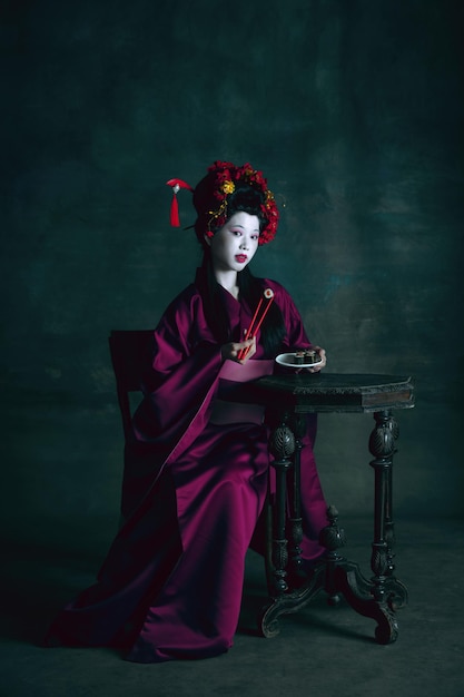 Young japanese woman as geisha on dark green background. Retro style, comparison of eras concept.