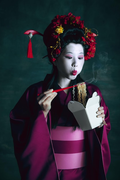 Young japanese woman as geisha on dark green background. Retro style, comparison of eras concept.