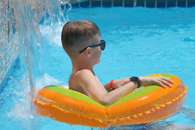 Young joyful child boy having fun swimming in inflatable air circle in swimming pool with blue water on warm summer day on tropical vacations Summertime activities concept