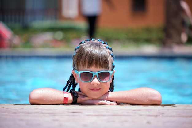 Young joyful child girl resting on swimming pool side with clear blue water on sunny summer day Tropical vacations concept