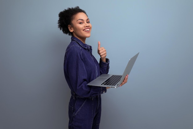 Young joyful hispanic business woman with fluffy hair dressed in a blue denim suit works in the