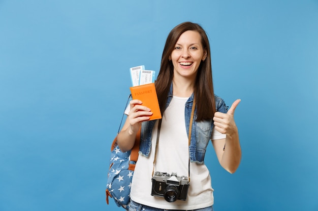 Young joyful woman student with retro vintage photo camera on neck hold passport, boarding pass tickets showing thumb up isolated on blue background. Education in university abroad. Air travel flight.