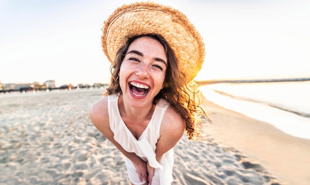 Young joyful woman in white shirt wearing hat smiling at camera on the beach