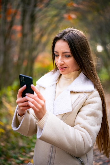 Young lady in autumn park with phone Woman portrait on beautiful outdoor nature